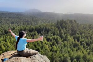Young Woman sitting on strawberry rock with her arms stretched out over the forest